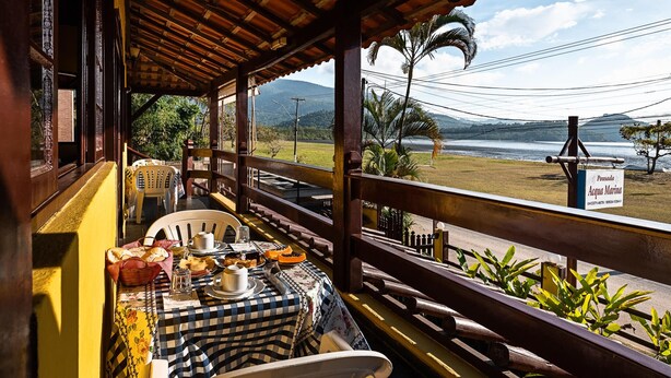A dining area with a table set for two, overlooking a scenic view of a body of water and mountains. - POUSADA ACQUA MARINA (Paraty)