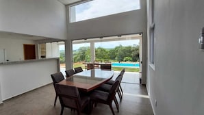 A modern interior with a large dining table, chairs, and a view of a swimming pool and greenery outside. - Casa Petronella (Pardinho)