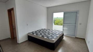 Quarto com cama, escada, porta e janela com vista para vegetação.