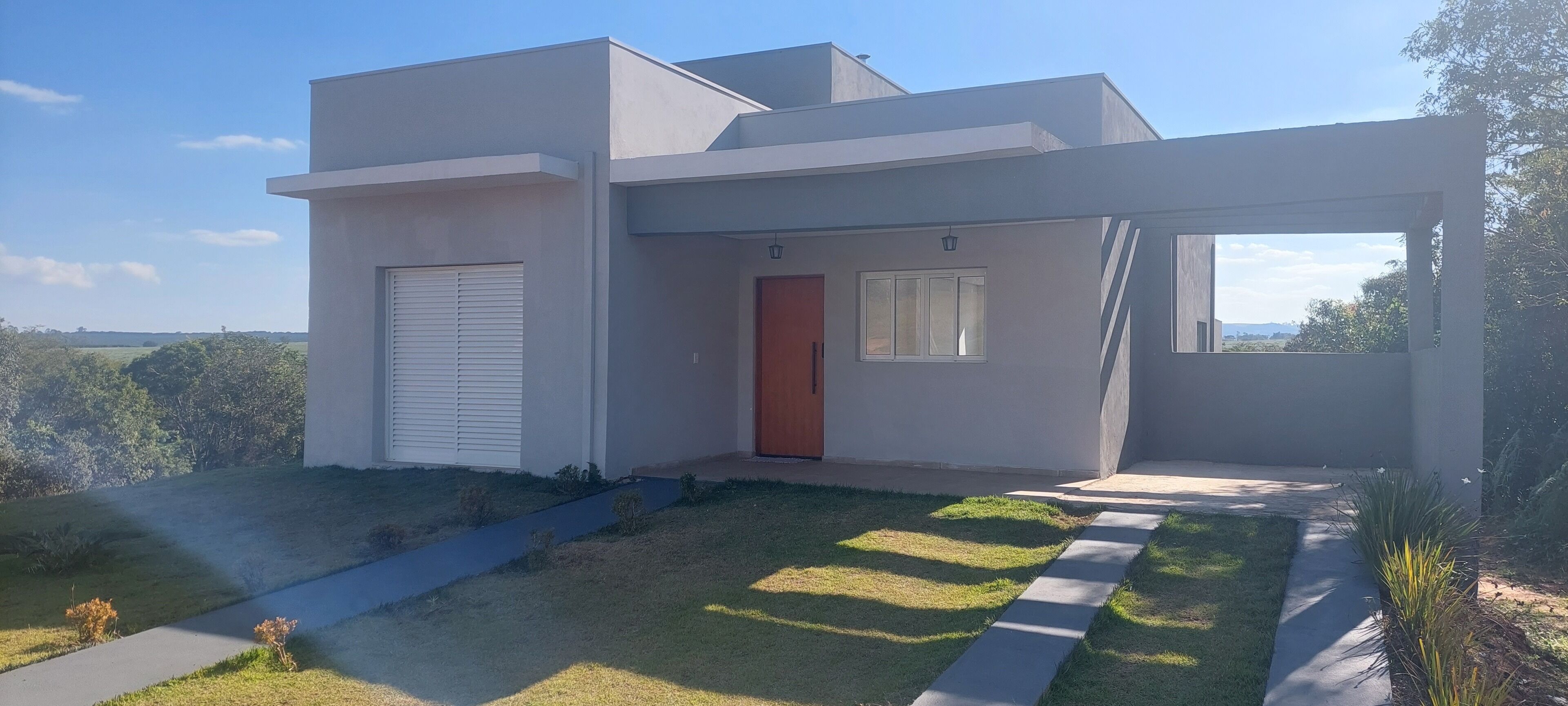 Una casa moderna de dos pisos con techo plano, puerta roja y un amplio ventanal en el segundo piso.