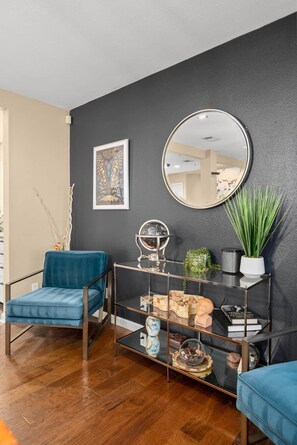 A modern living room with a blue armchair, a glass coffee table with decorative items, a round mirror, and a potted plant. - Secluded Half Acre Gem w/ Private Pickleball Court (Austin)