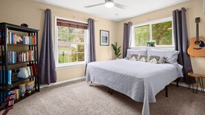 Ein Schlafzimmer mit einem Bett, einem Bücherregal, einem Fenster mit Vorhängen und einem Deckenventilator.