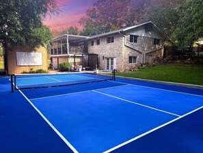 Una cancha de tenis al aire libre con una red, rodeada por un edificio de piedra con balcón.