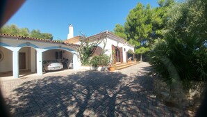 A house with a paved driveway, a car parked in the garage, and a garden with trees and plants. - Cozy villa with sea view. (Peschici)