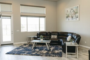 A living room with a leather sofa, a coffee table, and a rug. There are windows and a door visible. - Fully-Furnished Home in Beaumont, CA (Beaumont)