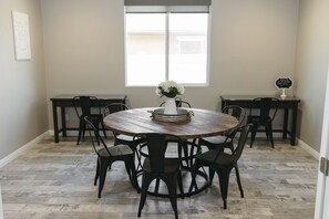 A dining area with a round wooden table surrounded by chairs, a vase with flowers, and a window with blinds. - Fully-Furnished Home in Beaumont, CA (Beaumont)