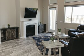 A living room with a fireplace, a television mounted above it, a coffee table, and a leather sofa. - Fully-Furnished Home in Beaumont, CA (Beaumont)
