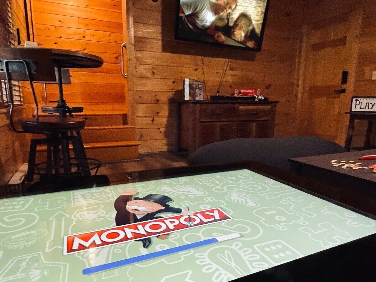 Huoneessa on pöydällä Monopoly-lautapeli, televisio ja seinät ovat puuta.