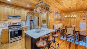 A wooden cabin interior with a kitchen, dining area, and a central island with bar stools. - Ellijay River Access (Trout!) | Hot Tub| Firepit | Games | Dogs Welcome! (Cherry Log)