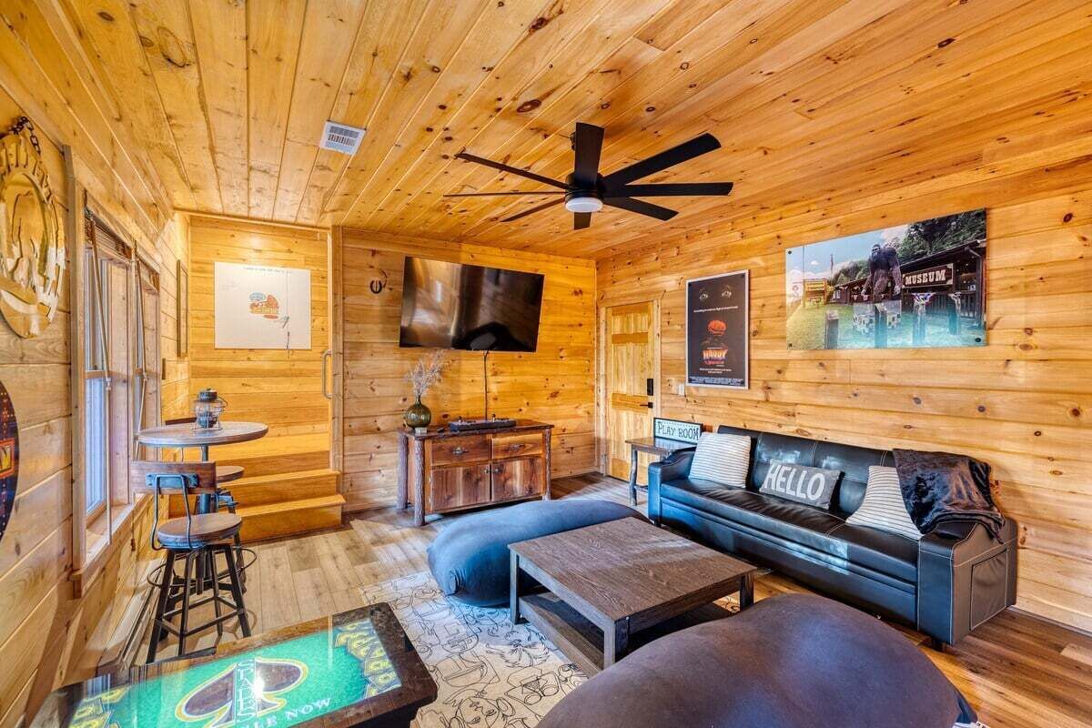 A cozy wooden cabin interior with a sofa, coffee table, and bar stools.