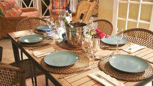 A dining table set with plates, cutlery, and a bottle of wine, surrounded by wicker chairs. - Bay House - 3 bedroom Villa, private pool and garden, near beaches (Saint Mary)