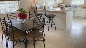 A modern kitchen with white cabinets, a central island, and a dining area with a table and chairs. - Bay House - 3 bedroom Villa, private pool and garden, near beaches (Saint Mary)