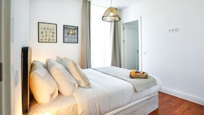 Una cama bien tendida con una mesita de noche, una lámpara colgante y un cuadro en la pared.