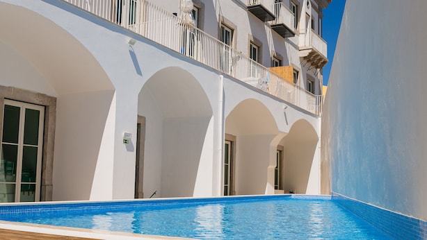 Una piscina con cubierta de madera, arcos blancos y un balcón con barandillas.