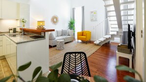 Un espacio habitable moderno con cocina, sofá, una silla amarilla y una escalera.