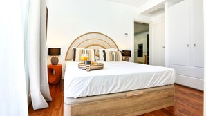 Quarto moderno com cabeceira de madeira, cama com edredom branco, mesa de cabeceira com abajur e bandeja com copo de suco de laranja.