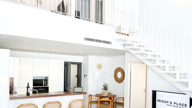 Uma sala de estar espaçosa, com um sofá, uma TV e uma cozinha ao fundo.