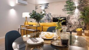 A dining area with a glass table, plates, cutlery, and a dessert. There is a sofa and a television in the background. - Savannah Apartment, by Bolhão Residences (Porto)