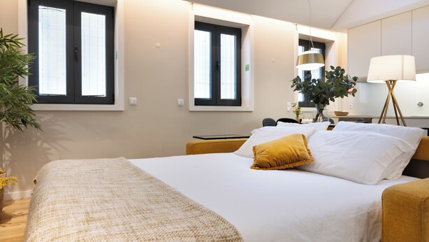 A hotel room with a bed, a desk, a lamp, and a window with blinds. - Savannah Apartment, by Bolhão Residences (Porto)