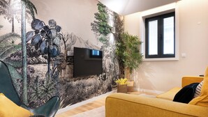 A living room with a mural, a flat-screen TV, a yellow sofa, and a green chair. - Savannah Apartment, by Bolhão Residences (Porto)