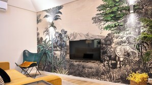 A living room with a large mural, a flat-screen TV, a yellow sofa, and a wicker basket with yellow flowers. - Savannah Apartment, by Bolhão Residences (Porto)