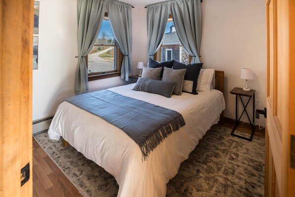 A bedroom with a large bed, two bedside tables, and a view of a house through the window.