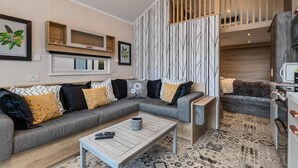 A modern living room with a sectional sofa, a coffee table, and a staircase leading to an upper level. - The Escape - Luxury Pod, Close to Beach (Wisemans Bridge)