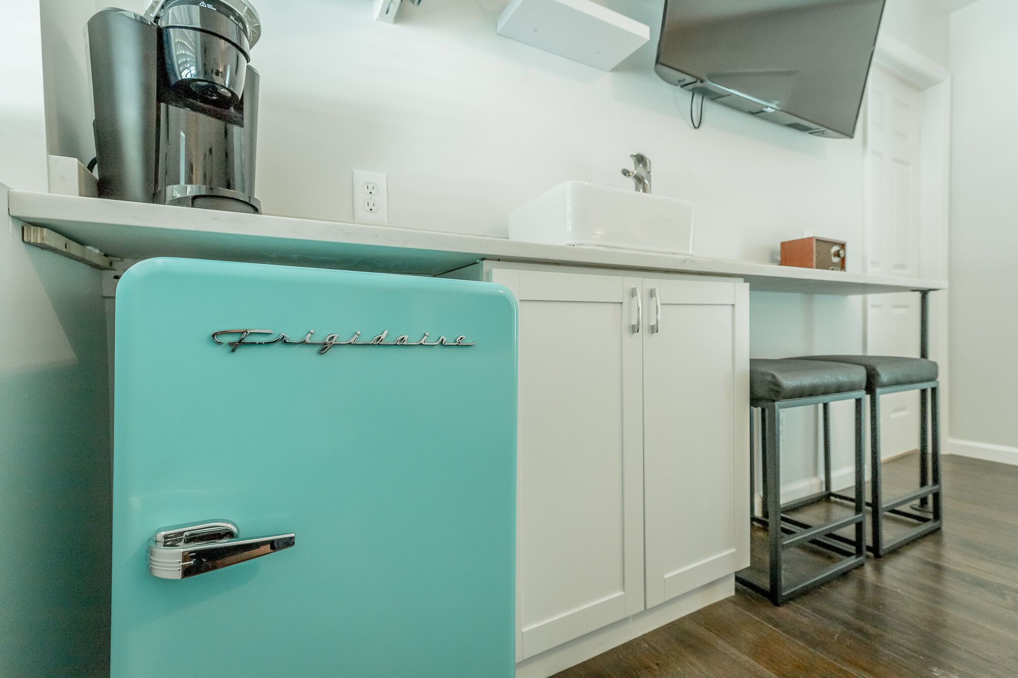 Une cuisine avec un réfrigérateur turquoise, une machine à café, un évier et un tabouret de bar.