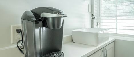 Una cafetera sobre una encimera blanca en una cocina moderna con ventana y armarios blancos.