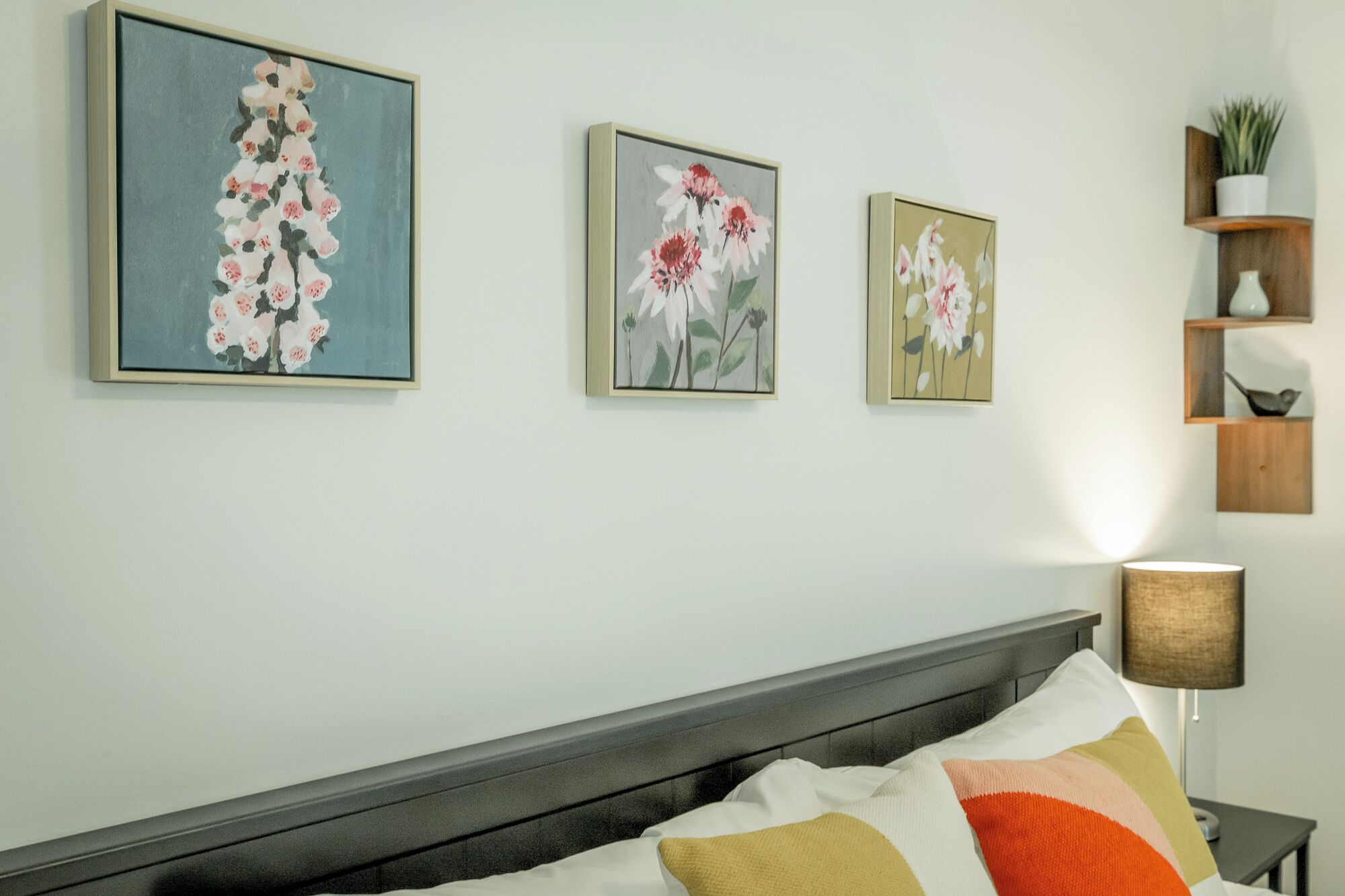 A bedroom with a bed, a nightstand, and three wall-mounted floral paintings.