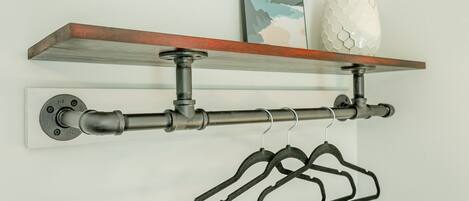 Un portaobjetos metálico con un estante de madera encima, que sostiene un pequeño florero y un cuadro enmarcado.