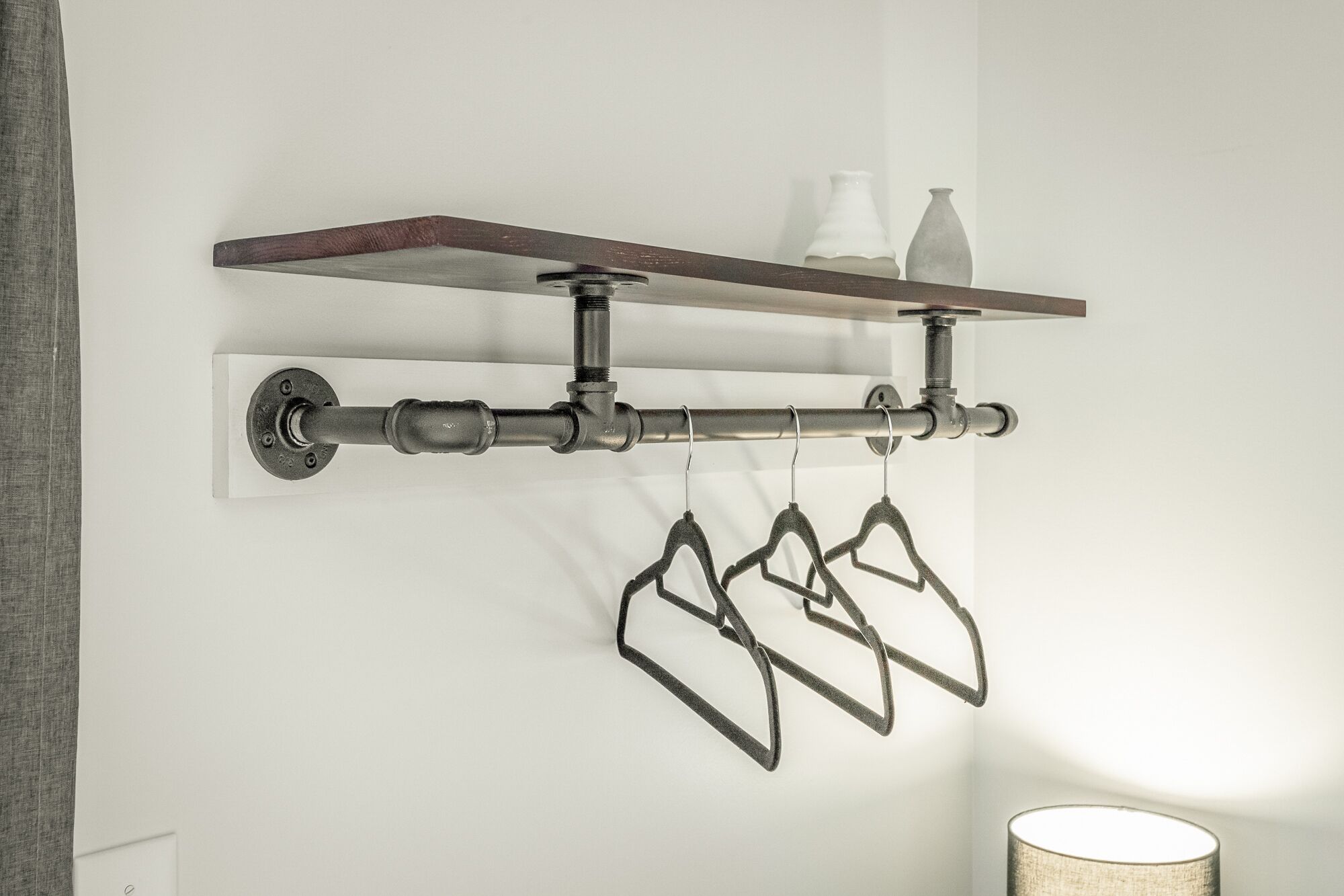 Uma prateleira fixada na parede com estrutura de metal, exibindo duas garrafas brancas e dois cabides pretos.
