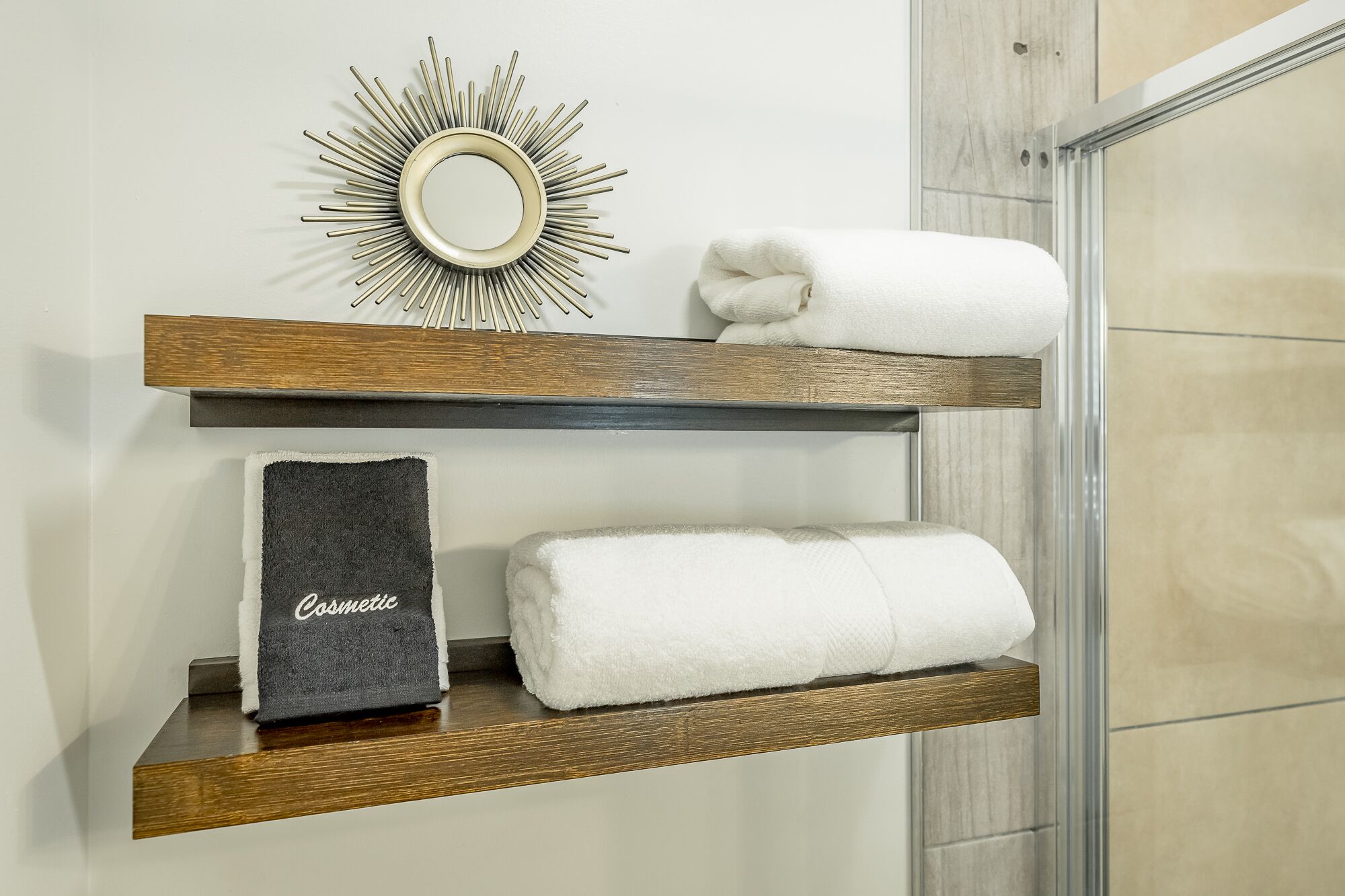Une salle de bain avec des étagères en bois où sont rangées les serviettes et un miroir décoratif.