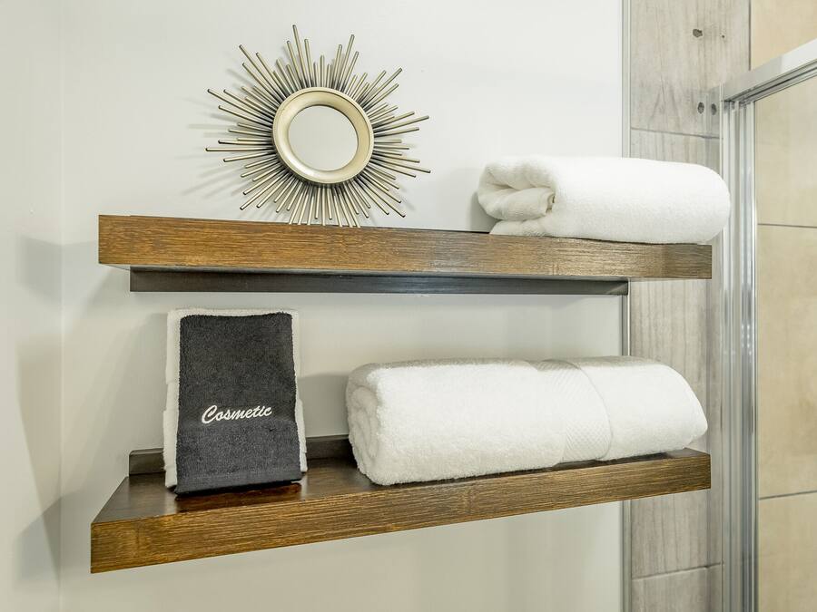 Une salle de bain avec des étagères en bois où sont rangées les serviettes et un miroir décoratif.