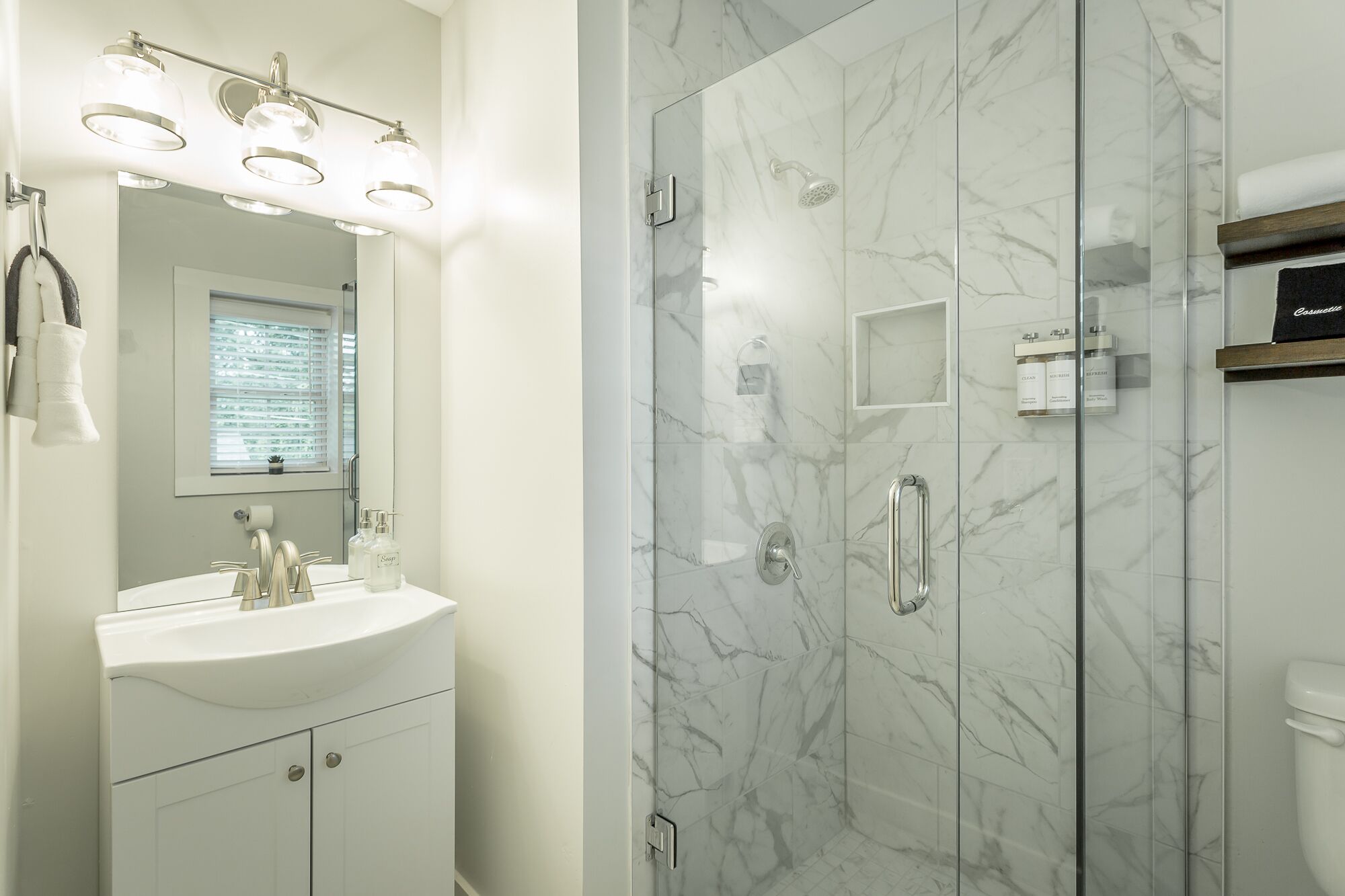 A modern bathroom with a marble shower enclosure, a vanity with a sink, and a mirror above the sink.