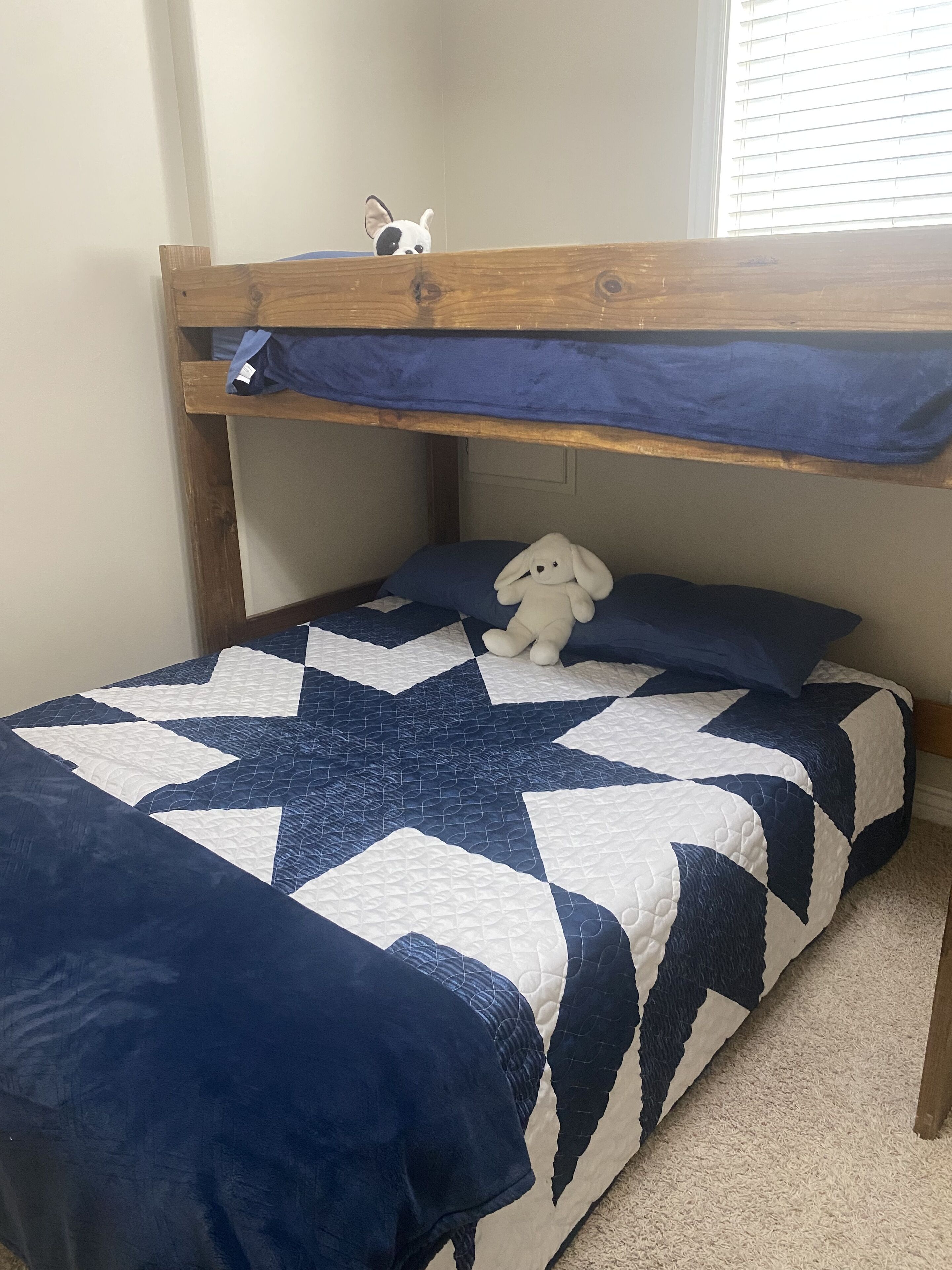 A bunk bed with a star-patterned quilt, a plush toy on the lower bunk, and a window with blinds.
