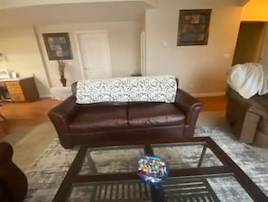 Un salon avec un canapé en cuir marron, une table basse en verre agrémentée d’un objet décoratif et un coussin à motifs.