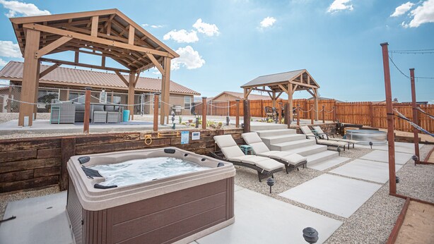 Een bubbelbad, lounge stoelen en houten pergola's in een achtertuin.