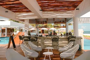 Uma área de bar à beira da piscina com espreguiçadeiras e guarda-sóis, com vista para a piscina e o oceano.
