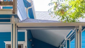 A blue house with a yellow door, white railings, and a wooden front porch. - The Sunset|Pet-Friendly Downtown 1BR · Easy Entry · Patio Access · (Eugene)