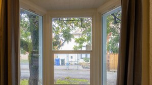 A room with a bay window, a view of a tree, and a fence in the background. - The Sunset|Pet-Friendly Downtown 1BR · Easy Entry · Patio Access · (Eugene)
