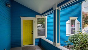 A house with blue siding, a yellow door, and a window with white shutters. - The Sunset|Pet-Friendly Downtown 1BR · Easy Entry · Patio Access · (Eugene)