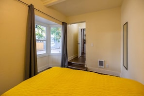 Ein Zimmer mit einem Bett, einem Vorhangfenster, einer Tür und einer Treppe, die zu einem anderen Raum führt.