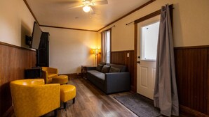 A room with a ceiling fan, a sofa, two armchairs, a small table, and a door with curtains. - The Sunset|Pet-Friendly Downtown 1BR · Easy Entry · Patio Access · (Eugene)