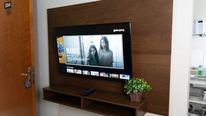 A flat-screen TV mounted on a wooden wall with a remote control and a small potted plant on a shelf below. - CONDOMÍNIO SONHARE - 104 (Anapolis)