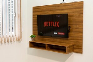 Un televisor de pared con el logotipo de Netflix, una planta pequeña y un estante de madera debajo.