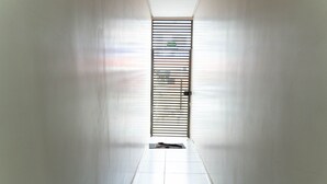 Un pasillo con una puerta al final, piso de baldosas y una verja metálica con un letrero encima.