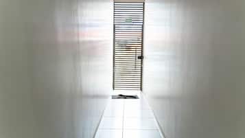 Un pasillo con una puerta al final, piso de baldosas y una verja metálica con un letrero encima.