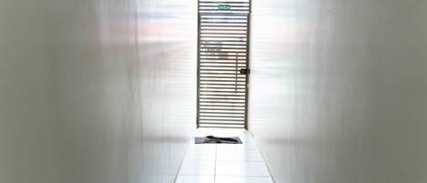 A corridor with a door at the end, a tiled floor, and a metal gate with a sign above it.