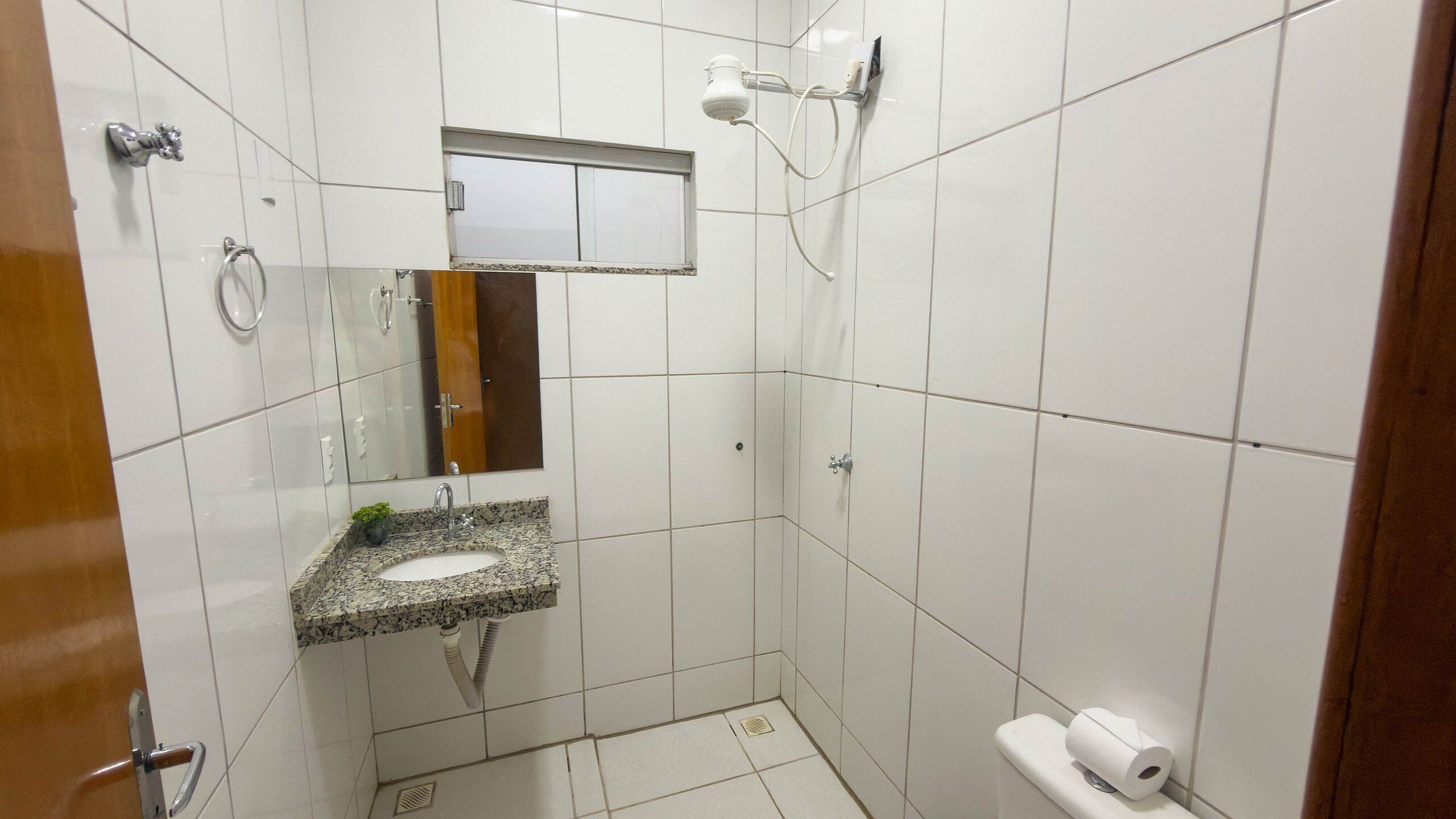 Um banheiro pequeno, com azulejos, pia, espelho e chuveiro.